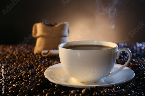 Cup of hot coffee among coffee beans on dark background