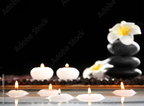 Spa still life with stones  candles and flowers in water on black background