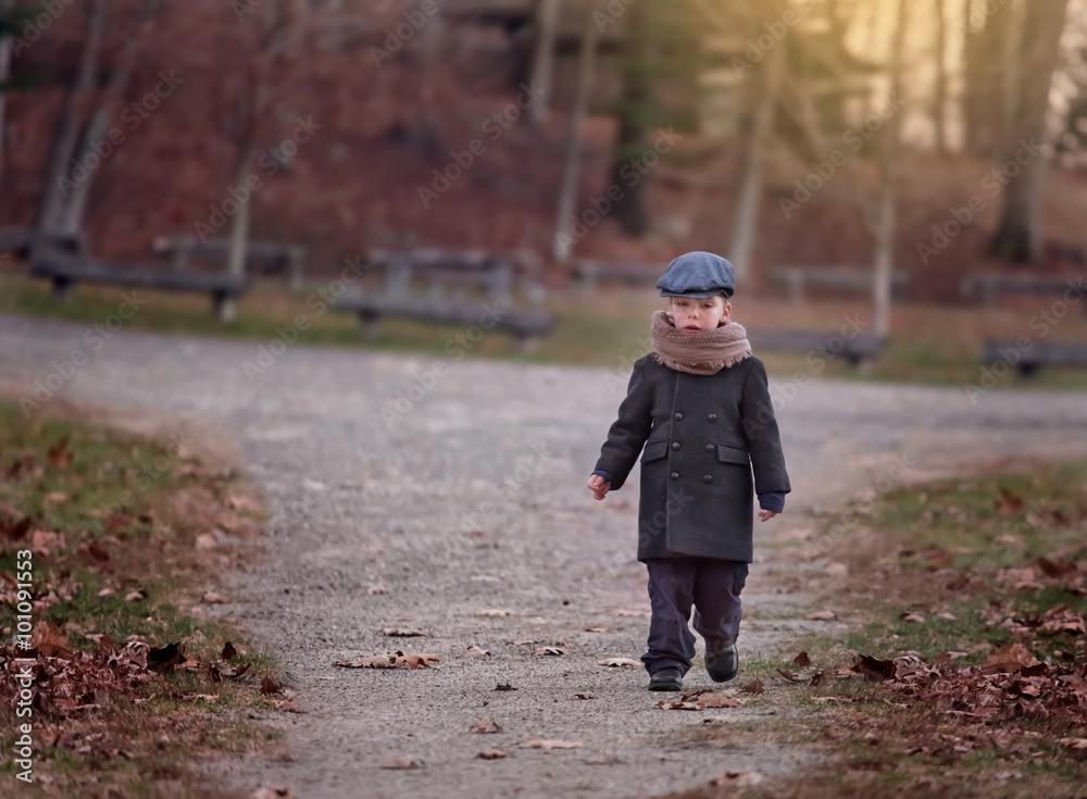 Fototapeta premium serious little boy wearing a hat walking on a path in a park on a chilly day