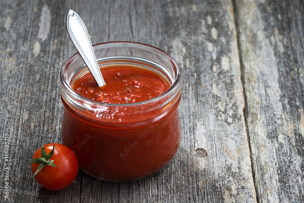tomato sauce in a glass jar on a wooden background, closeup tomato sauce in a glass jar on a wooden background, closeup