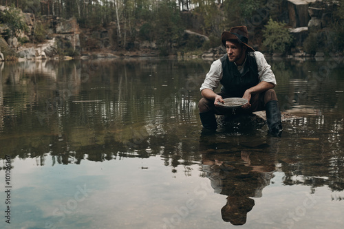 unshaved golddigger washes gold in the lake with rocky bank 