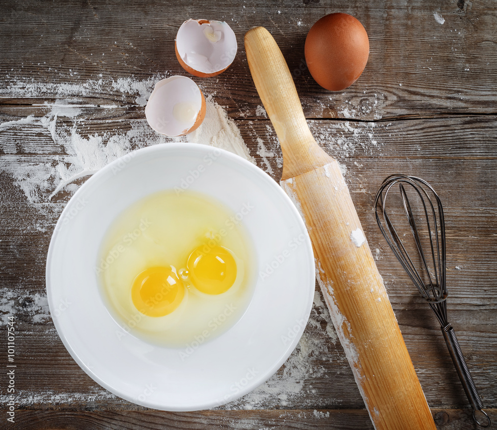 Cooking or baking. Still life with eggs, raw eggs in a dish, eggshells, flour, rolling pin and whisk on wooden background. Cooking or baking. Still life with eggs, raw eggs in a dish, eggshells, flour, rolling pin and whisk on wooden background.