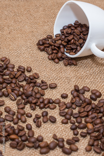 coffee beans on sackcloth white cup on a desk brown texture close a lot of grain