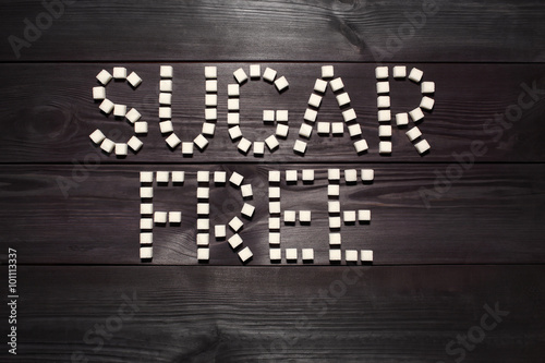 The words 'sugar free', built from white cubes pieces of sugar on background  of panel from vintage wooden boards black color in high contrast dramatic lighting  'Hard light'