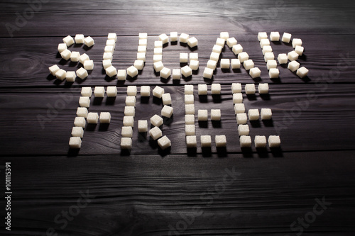 The words 'sugar free', built from white cubes pieces of sugar on background  of panel from vintage wooden boards black color in high contrast dramatic lighting  'Hard light'. Selective focus
