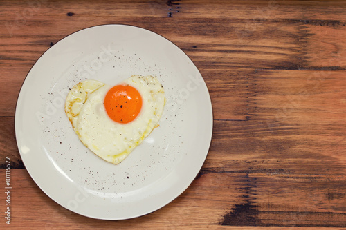 fried egg heart on white plate on brown wooden background