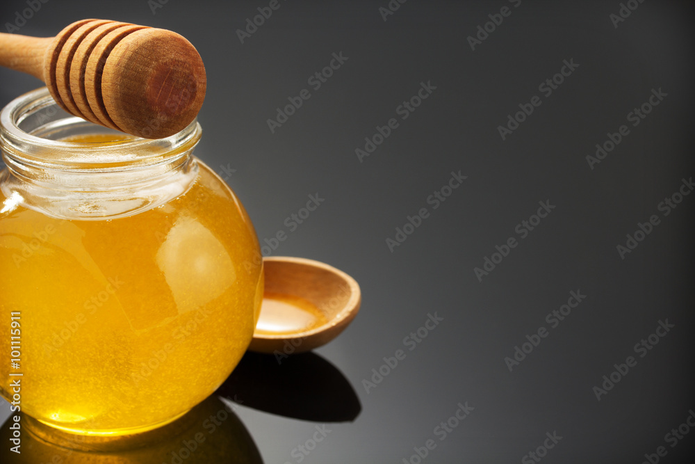 glass jar of honey and stick on black glass jar of honey and stick on black