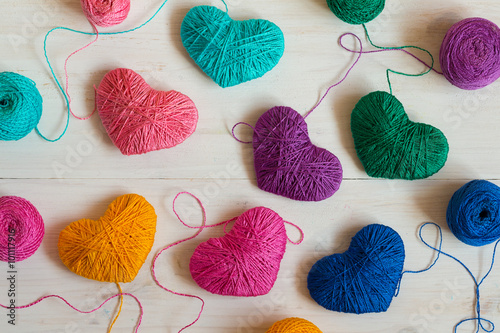 Multicolored Hearts with a balls of thread on white wooden backg photo