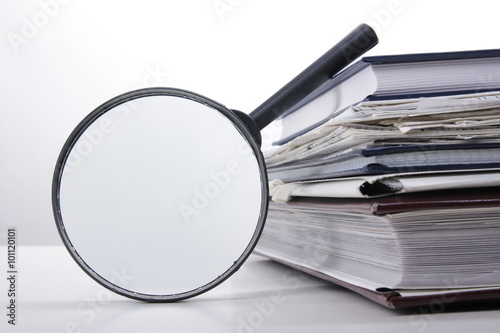 Stack of books with magnifying glass. Search information.