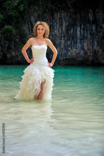blonde bride in fluffy hands on waist in shallow azure sea