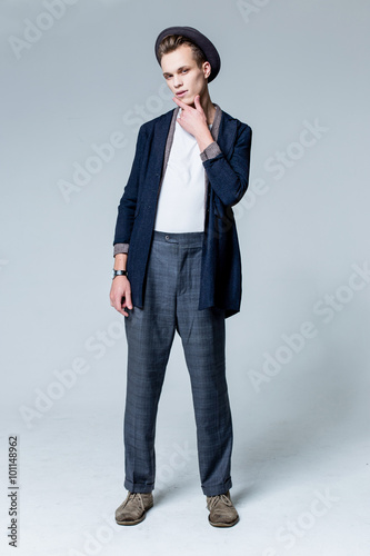 full length picture of a cool young man wearing black hat looking forward with a serious look