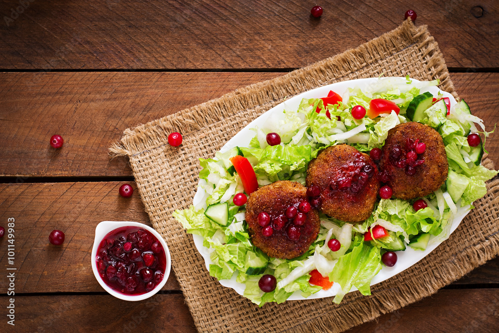 Juicy meat cutlets with cranberry sauce and salad on a wooden table in a rustic style. Top view