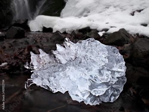 Beautiful big piece of ice with abstract cracks. Icicle bellow waterfall, stony and messy stream bank © rdonar