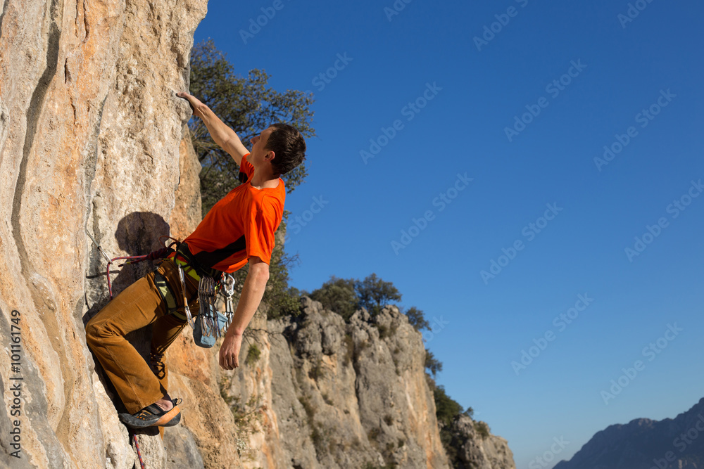 Young male rock climber on challenging route on cliff.