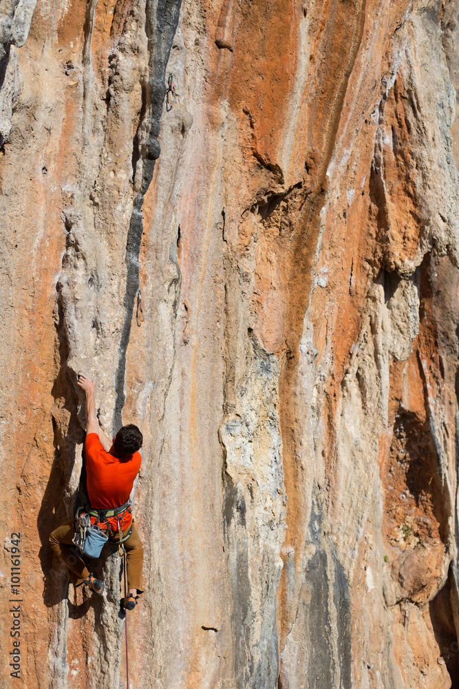 Fototapeta premium Young male rock climber on challenging route on cliff.