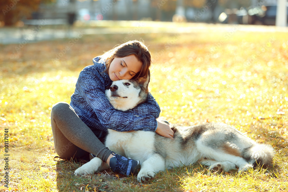 Happy young woman sitting with her dog on grass in park Happy young woman sitting with her dog on grass in park