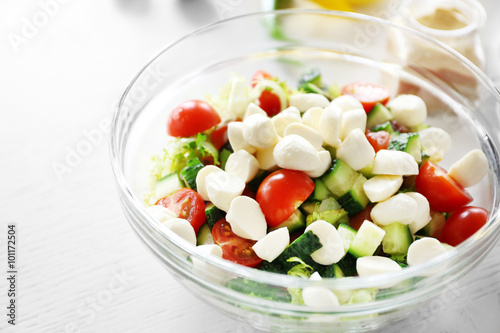 Tasty salad in glass dish on color wooden table background