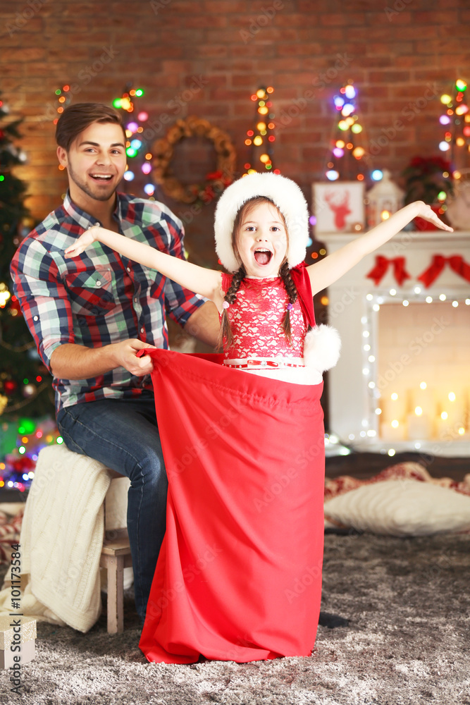 Obraz premium Funny little sister in Santa sack surprising her older brother on Christmas background