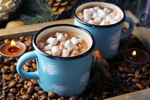 Two mugs of hot cacao with marshmallow on coffee beans