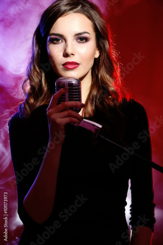 Beautiful singing woman on red background in the smoke, close up © Africa Studio
