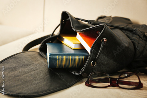 Fashion female backpack with books and glasses on a sofa, close up