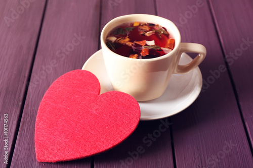 Cup of fruit tea on a limpet with red heart on wooden background closeup
