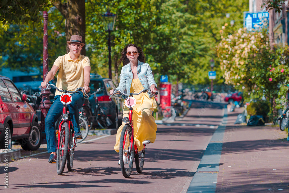 Obraz premium Young happy caucasian couple on bikes in old streets in Amsterdam