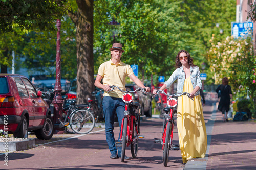 Canvas Print Young happy caucasian couple on bikes in old streets in Amsterdam