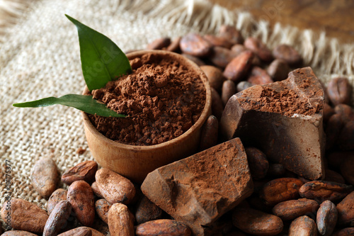 Bowl with aromatic cocoa powder and green leaf on a sacking, close up
