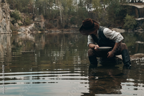 unshaved golddigger washes gold in the lake with rocky bank 