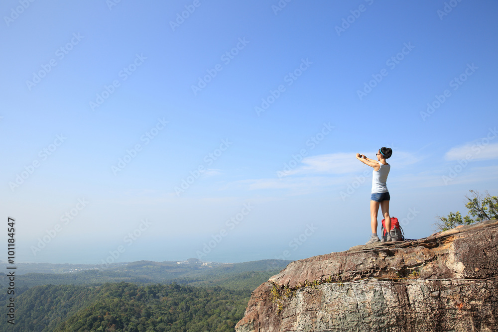 Obraz premium young woman backpacker taking photo with camera on mountain peak