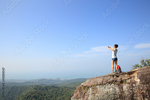 young woman backpacker taking photo with camera on mountain peak