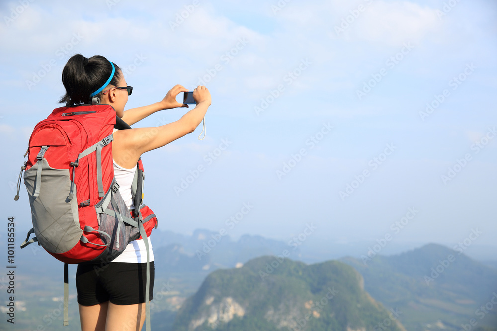 young woman backpacker taking photo with camera on mountain peak