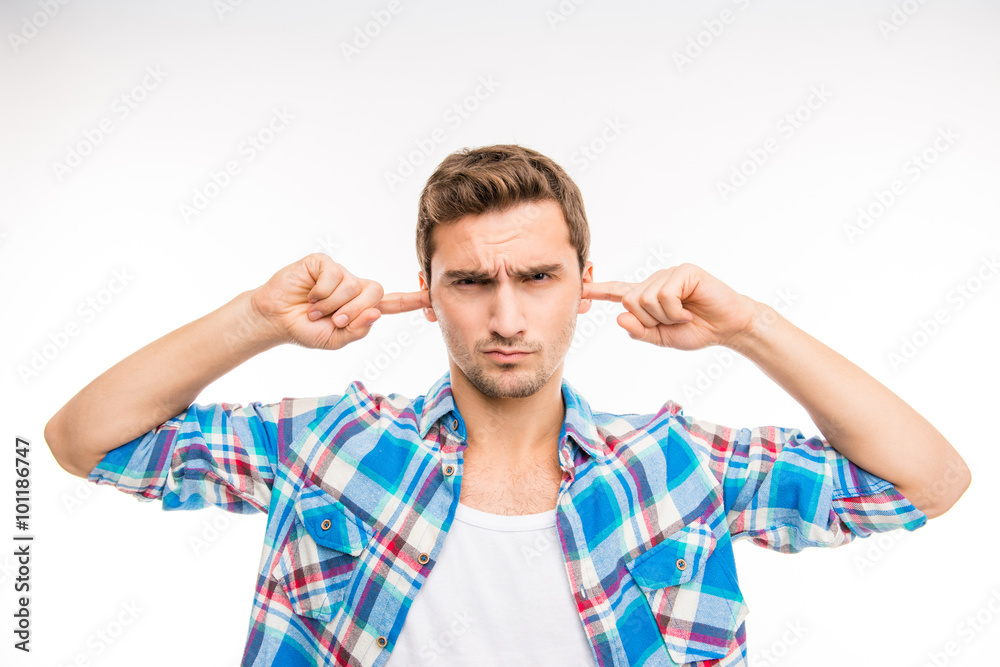 Cute young man closing ears and frowning Cute young man closing ears and frowning