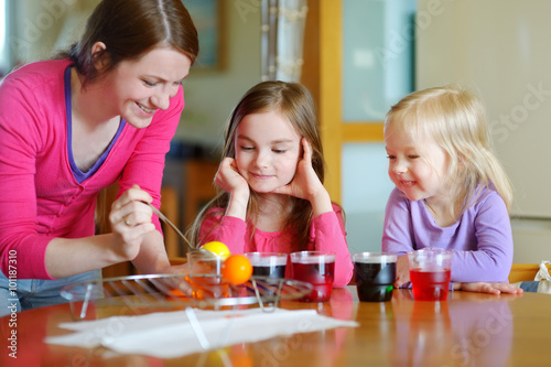 Young mother and her two daughters painting Easter eggs © MNStudio