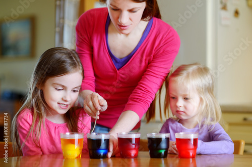 Young mother and her two daughters painting Easter eggs