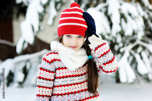 Adorable school aged kid girl in colorful sweater and hat playing in the snow on beauty winter day