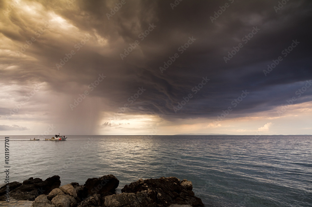 Fishing boat sailing away towards storm clouds on a calm sea