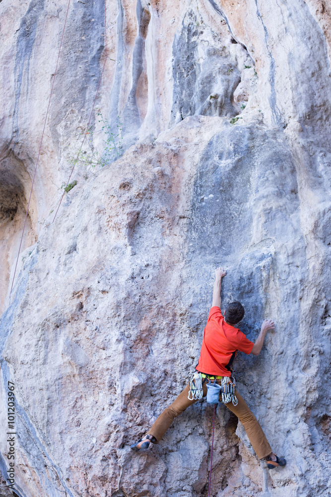 Young man climbing on a limestone wall with wide valley on the background Young man climbing on a limestone wall with wide valley on the background
