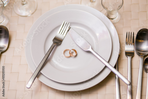 two rings on a plate with serving fork, spoon, knife. The concept of a wedding celebration at Banquet, restaurant. photo