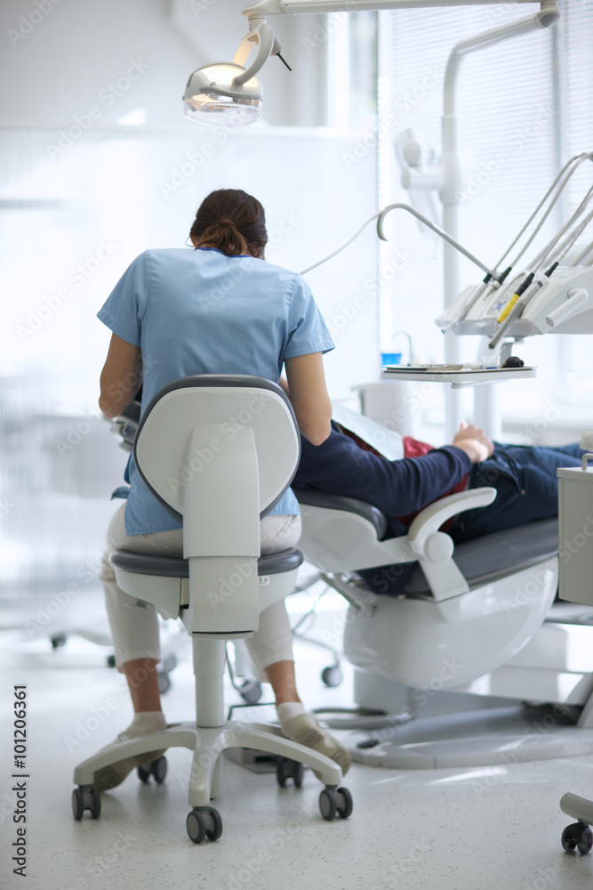 Fototapeta premium Rear view of a female doctor treating patient's teeth in a dental office