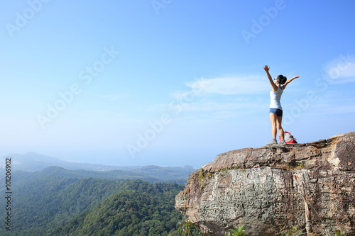 cheering young woman hiker open arms at sunrise mountain peak