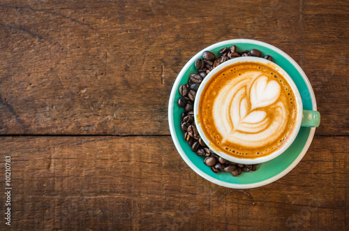 Latte hot coffee in green cup with latte art and roasted coffee beans. Wooden table background. Top view.