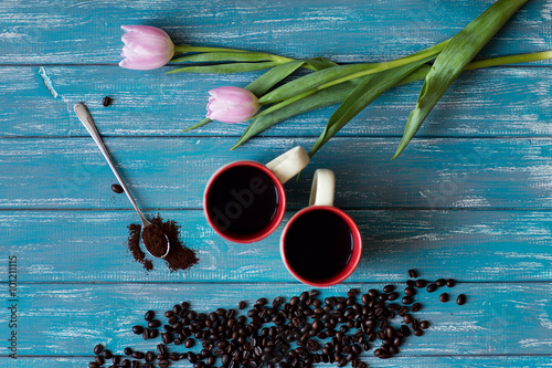 Selective focus coffee beans, pink tulips, and 2 cups of black American stand on a blue table photo