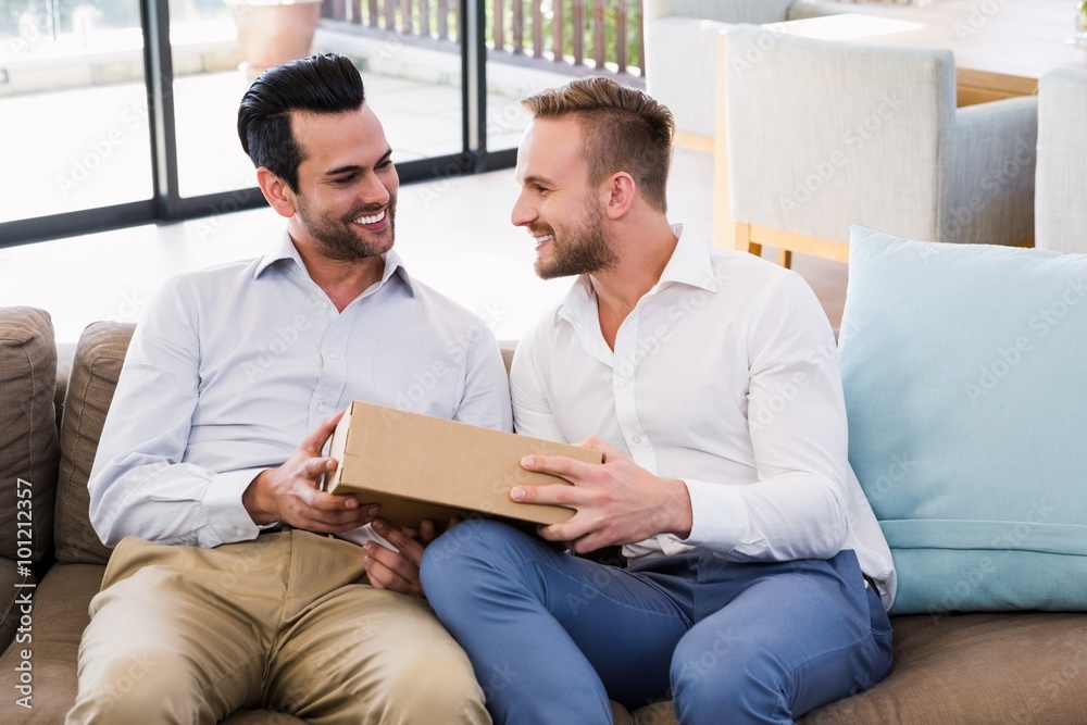 Smiling man offering gift to his boyfriend in living room 