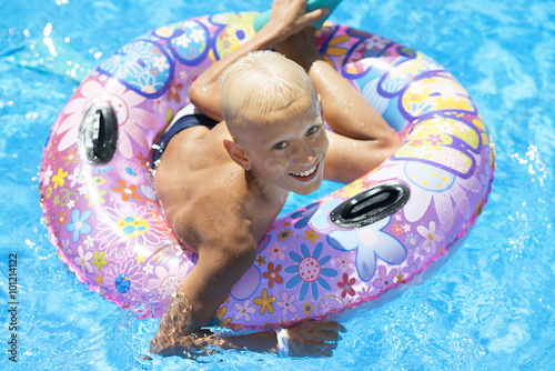 Młody chłopiec na wakacjach pływa w kole w basenie.
