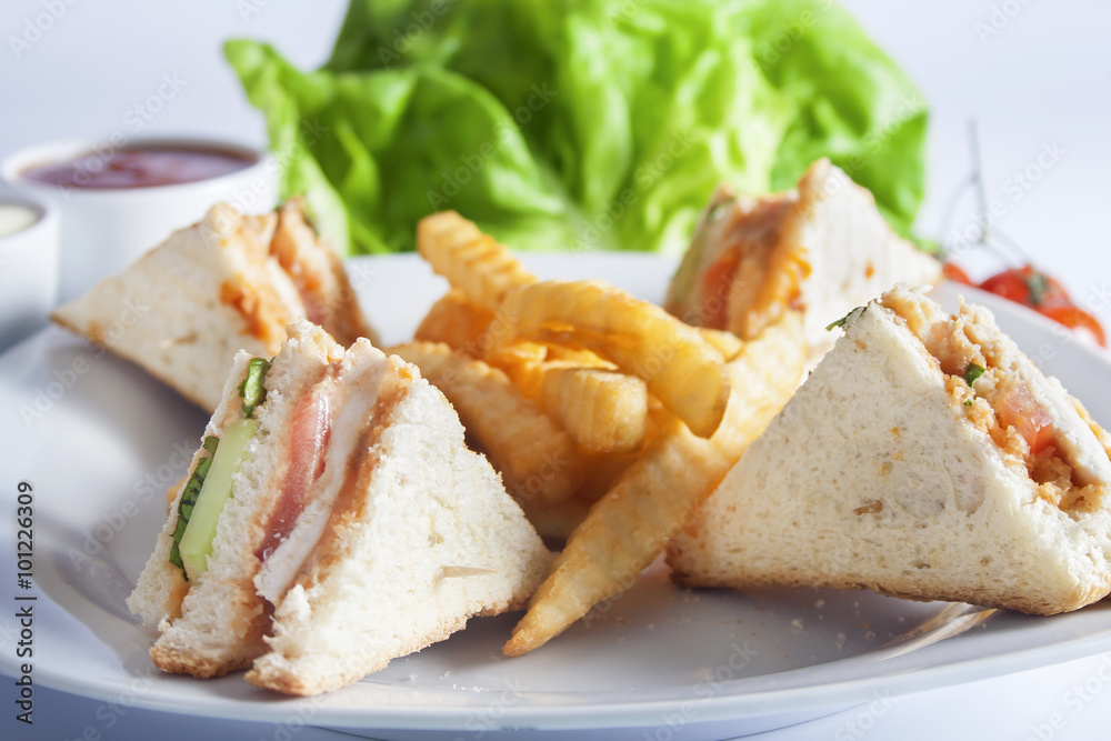 Club sandwiches with grilled chicken, tomato, lettuce, cheese, cucumber and dressing sauce, served on a white plate with french fries. Club sandwiches with grilled chicken, tomato, lettuce, cheese, cucumber and dressing sauce, served on a white plate with french fries.