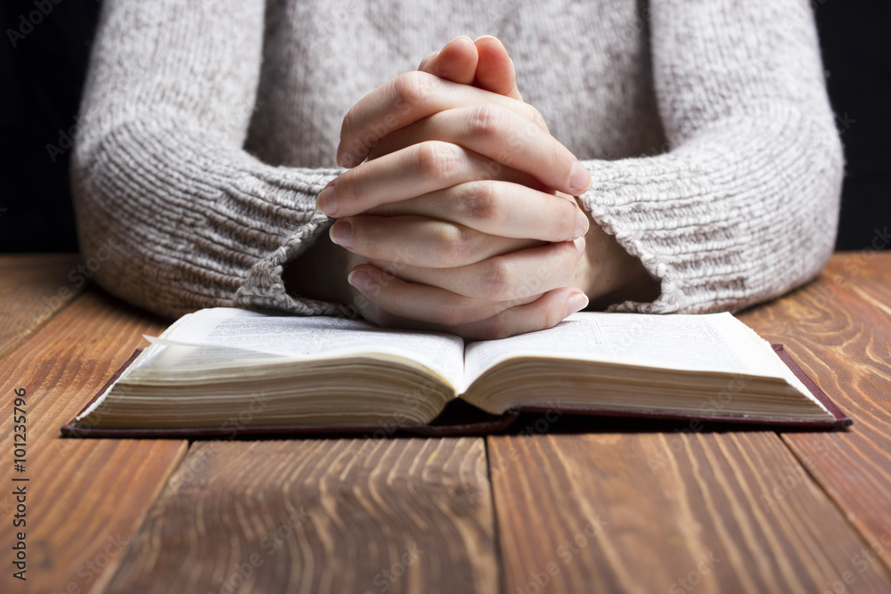 Woman hands praying with a bible in dark over wooden table Woman hands praying with a bible in dark over wooden table