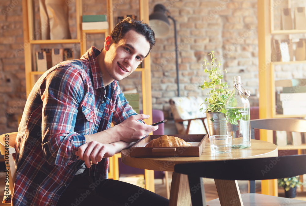 Young man sitting at a cafe, using a cell phone, drinking espresso Young man sitting at a cafe, using a cell phone, drinking espresso