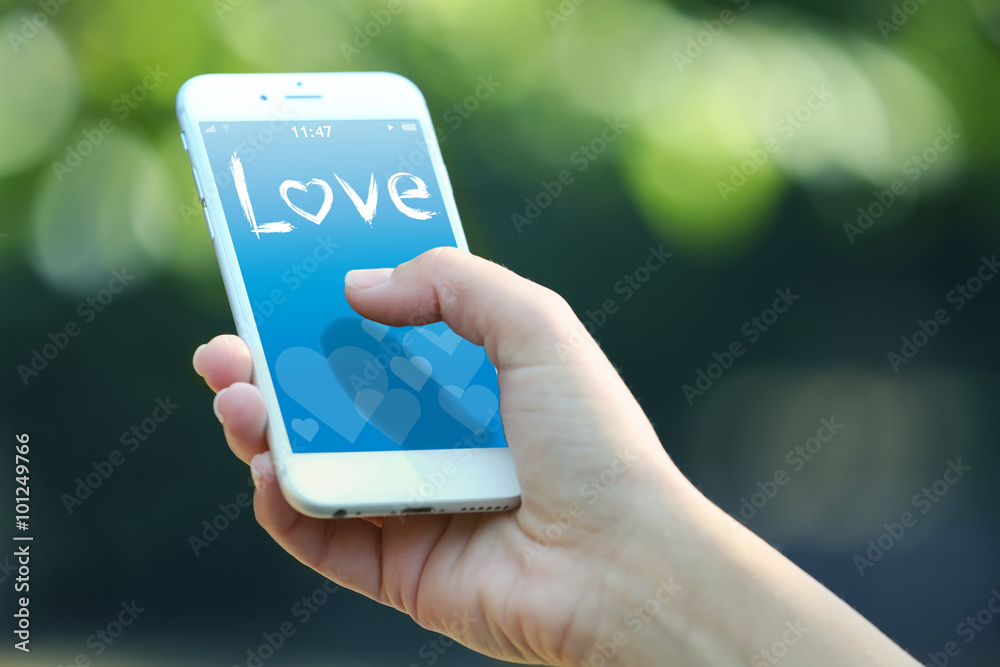Female hand holding a mobile phone with romantic screensaver, outdoors